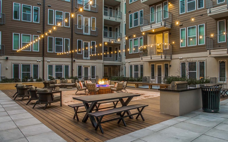 overhead stringed lighting brightens courtyard with grilling area, social seating areas and fire pit